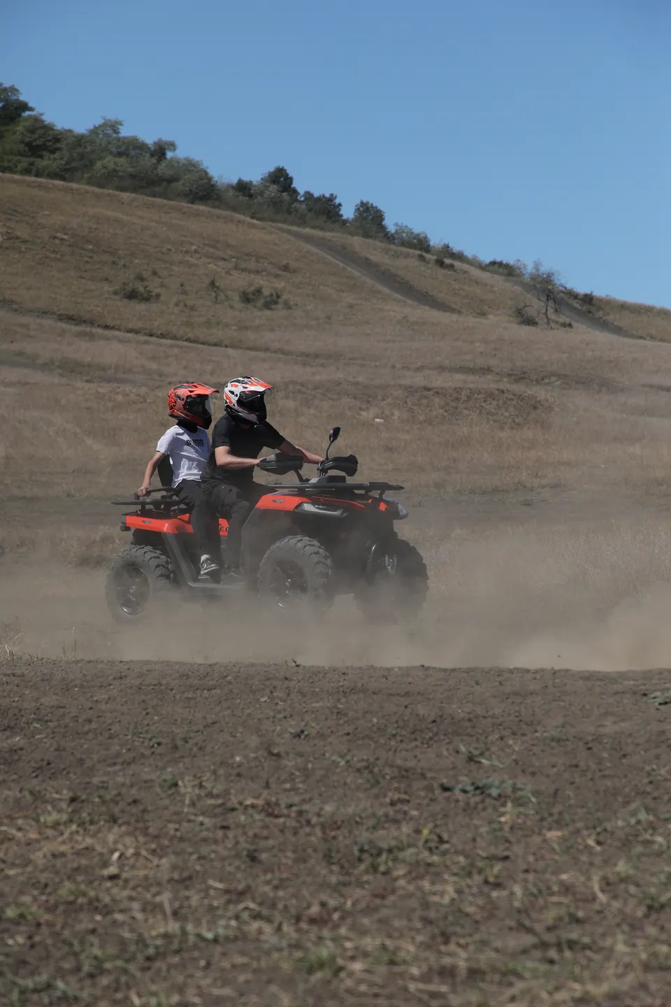 Doi oaspeți cu căști mergând cu ATV-ul prin praful traseului