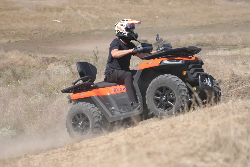Pilot cu cască urcând un deal pe un ATV portocaliu la DendroPark